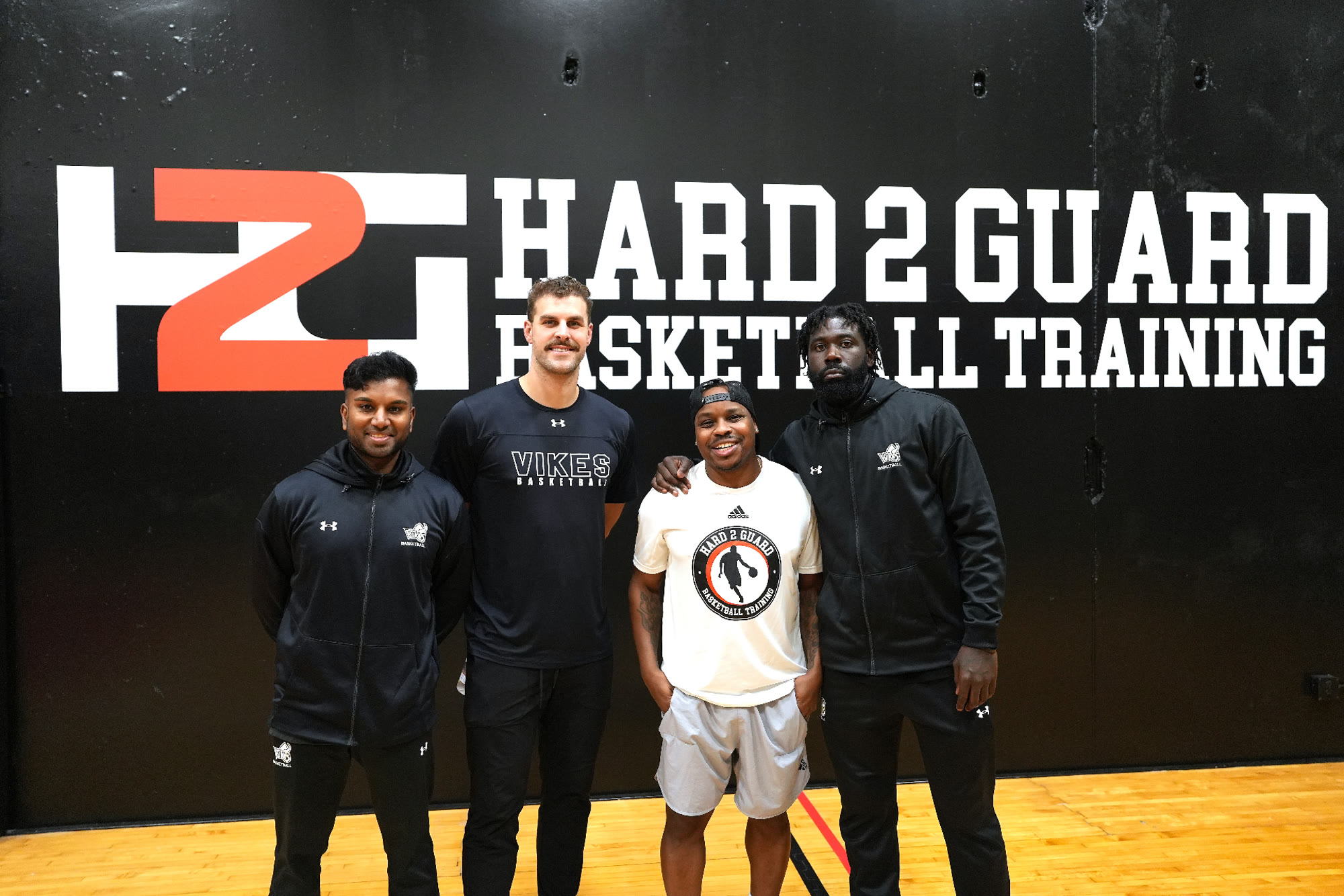 Coaches and players in front of the Hard 2 Guard logo.