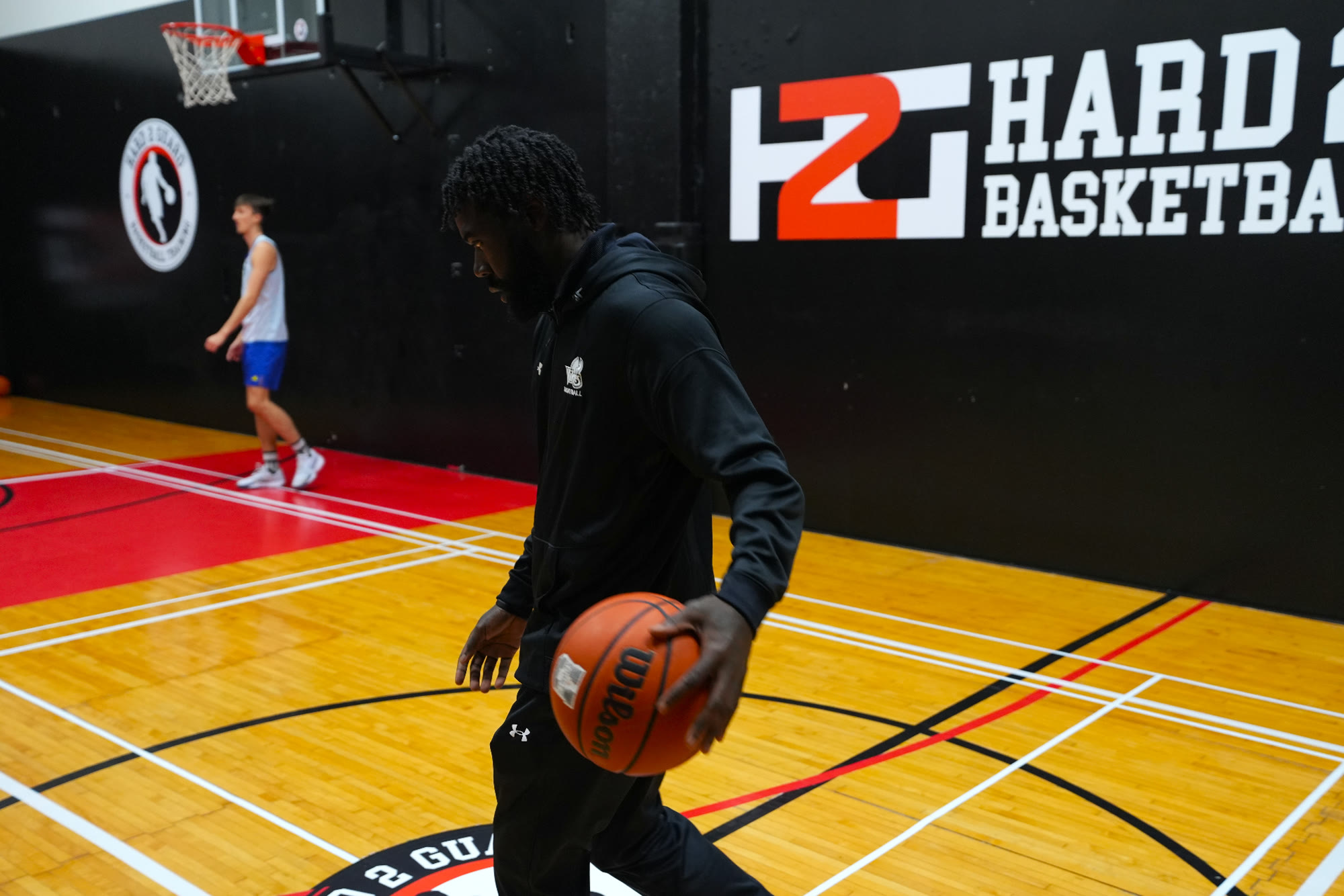Coach Steven Bennett dribbling in front of the Hard 2 Guard logo wall.